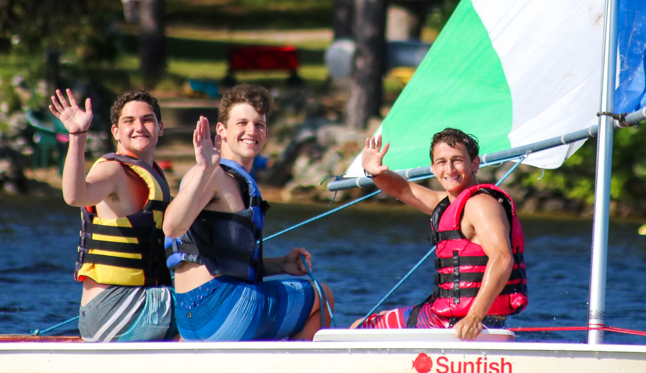 Three campers wave from sailboat